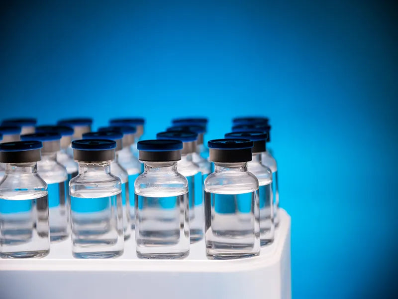 Row of clear glass vials with black caps on a white surface against a blue background