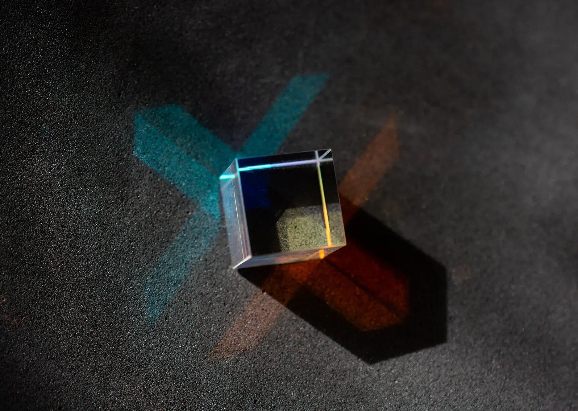 Transparent glass cube casting colorful blue and orange reflections on a dark textured surface